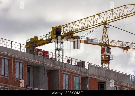 Tower cranes working on residential building construction site with concrete structure and brick walls under development in urban environment Stock Photo