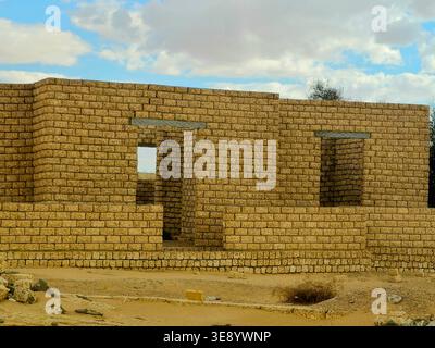 unfinished mud-brick walls of a building situated in a desert environment, the structure is built using compressed earth blocks or bricks made from so Stock Photo