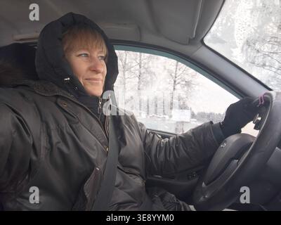 Woman takes a selfie while driving in a car, showing her focused expression in a cold environment. Stock Photo