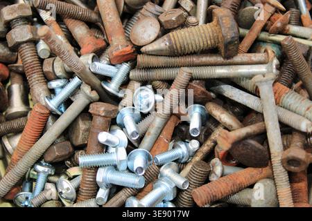 Various types of metal fasteners are mixed together on a surface in a workshop. The scene shows screws, bolts, and nuts scattered around in daylight. Stock Photo