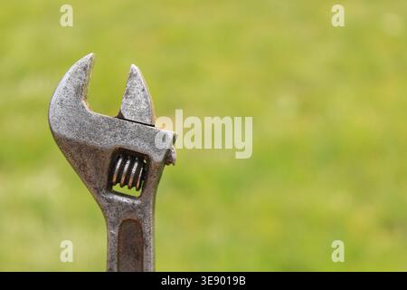 A person uses an adjustable wrench to tighten a metal pipe in a garden. The sun is shining, and green grass surrounds the repair area. Tools are scatt Stock Photo
