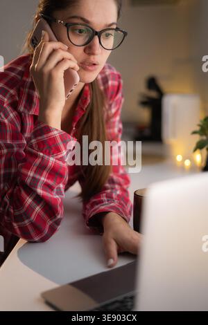 woman talking on smartphone using laptop at home, discuss contract with client. Stock Photo