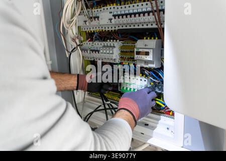 Close up of an electrician technician working with electrical panel and wires. Professional maintenance of a fuse box with circuit breakers in a resid Stock Photo