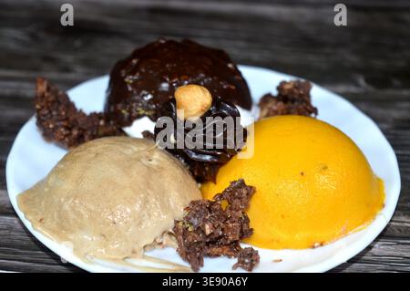 a dessert featuring three scoops of ice cream frozen dessert with different flavors, chocolate, vanilla, peanut butter and mango with toppings of clus Stock Photo
