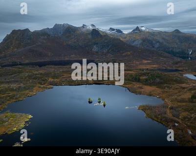 Aerial view of Lofoten islands with a dark mountain lake and snow-capped peaks under a dramatic cloudy sky Nordland, Norway. Stock Photo