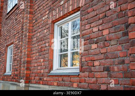 A white wooden window frame with glass panes is set into a red brick wall of an building. Stock Photo