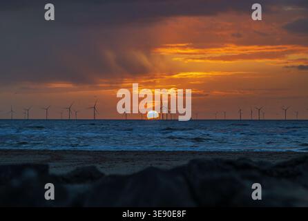 Golden sunset over the ocean with a line of River Mersey wind turbines silhouetted on the horizon, turbulent waves and dramatic clouds creating a mood Stock Photo