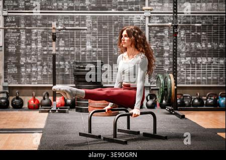 Athletic woman doing calisthenics L sit working out core and upper body in fitness center Stock Photo