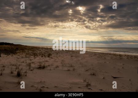 Sun rays breaking through clouds over sandy dunes and ocean shoreline, Long Island, New York Stock Photo