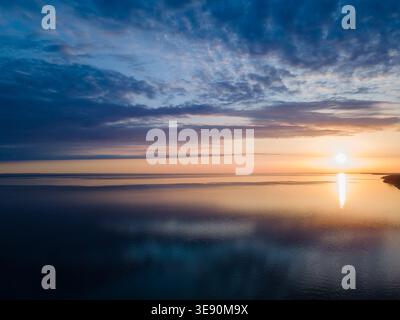 Aerial sunset over calm Long Island waters with colorful sky, soft clouds, and reflection creating peaceful coastal landscape Stock Photo