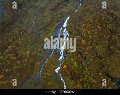 Aerial view of a cascading waterfall flowing down a steep rocky mountainside covered in vibrant autumn foliage and yellow trees in Senja, Troms, Norwa Stock Photo
