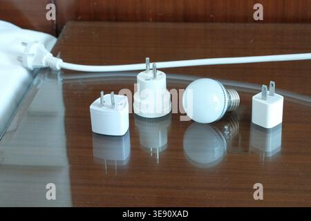 White light bulb and different international power plug adapters on bedside table. Concept of global travel, energy solutions, and electrical compatib Stock Photo