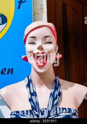 Vintage female mannequin head with wide laughing expression wearing a blue and white patterned scarf and strapless top outdoors lagos portugal algarve Stock Photo