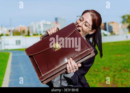 Businesswoman biting briefcase expressing frustration with work stress Stock Photo
