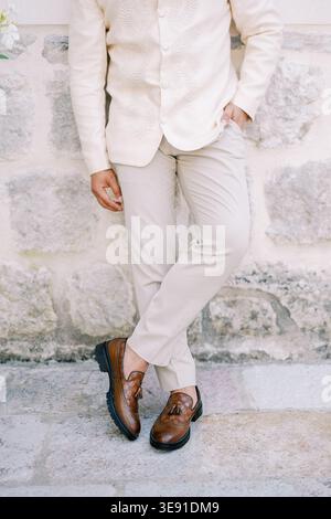 Man dressed in cream with relaxed stance. Wedding portrait showing groom by aged stone wall Stock Photo