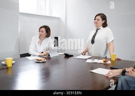 Smiling woman talking to colleague during breakfast business meeting at long table in modern office. Smiling, meeting, breakfast, woman, business. Stock Photo