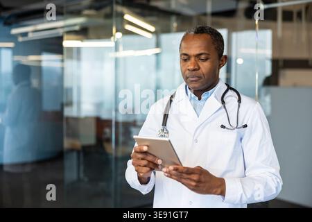 Experienced healthcare professional wearing a white coat and stethoscope using a digital tablet in a modern office environment, demonstrating medical technology and digital healthcare innovation Stock Photo