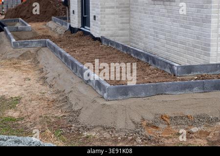 Landscape construction featuring gray concrete edging around a garden bed with freshly tilled soil and a brick house exterior in the background Stock Photo
