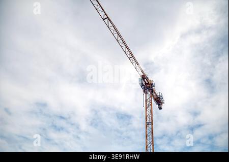 A construction crane lifts heavy materials at a site with clouds in the sky. Stock Photo