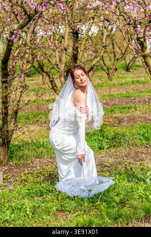 Bride posing in orchard during spring with umbrella Stock Photo
