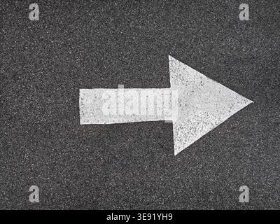 White directional arrow painted on dark asphalt surface. Simple, straight forward marking of direction. Stock Photo