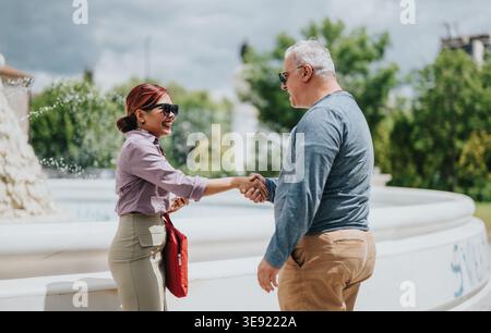 Business handshake between colleagues meeting outdoors by a fountain in a casual professional greeting Stock Photo