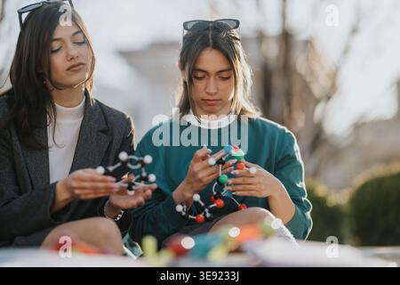 Two students examining colorful molecular models outdoors while studying chemistry and collaborating Stock Photo