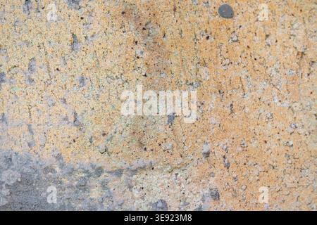 Rough weathered concrete wall surface displaying a textured background with varying shades of yellow brown, tan, and gray, indicating age and natural Stock Photo