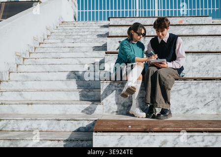 Two students studying together on marble stadium steps, collaborating and taking notes outdoors Stock Photo