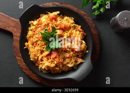 Stewed cabbage sauerkraut on black background, top view. Braised kraut side dish. Homemade finely cut white cabbage stew or crauti. Stock Photo