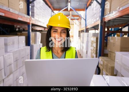 Smiling Hispanic woman logistics worker using laptop in warehouse facility Stock Photo