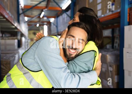 Two smiling warehouse workers embracing standing in stockroom Stock Photo