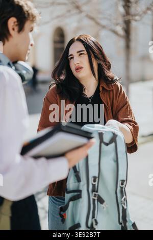 Female student talking to classmate while holding backpack on college campus in spring Stock Photo