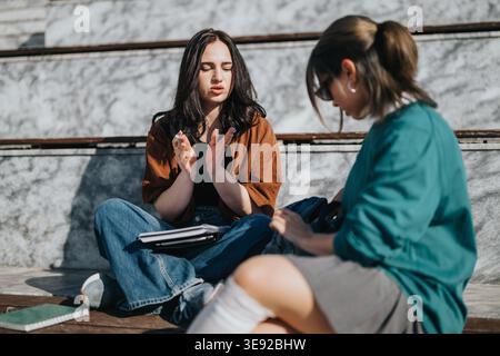 Two young women studying and discussing notes while sitting outdoors on steps Stock Photo