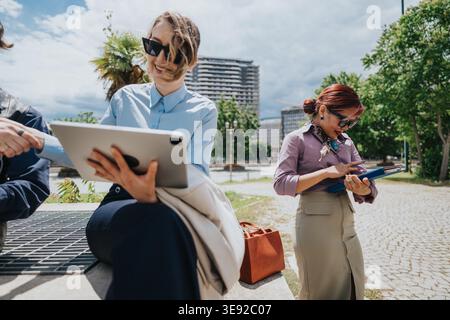 Business coworkers collaborating outdoors using tablet and clipboard in urban park setting Stock Photo