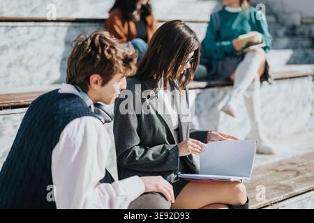 Students studying together on outdoor campus steps reviewing notes and discussing schoolwork Stock Photo