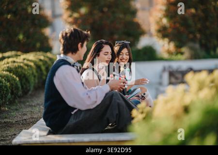 Three students sitting outdoors studying and chatting on a sunny university campus in spring Stock Photo