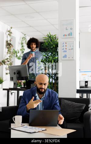 Arab entrepreneur presenting business plan to team during video conference call using laptop. Executive manager discussing product launch in videocall while sitting on couch in coworking space Stock Photo