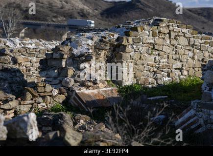 ancient stone and brick ruins of an antique city under bright sun with a modern highway bridge and truck in the blurred background. Stock Photo