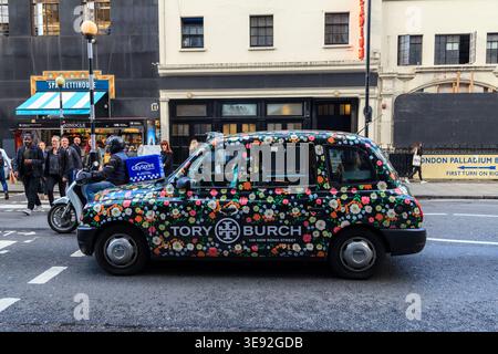 A London black cab wrapped in a colourful Tory Burch floral advertisement drives past the London Palladium in the West End, England Stock Photo