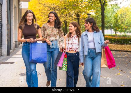 Four young women friends shopping and walking on city street in autumn Stock Photo