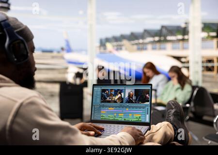 Black videographer reviewing film montage and editing in post production, seated in airport lounge before boarding. International travel with nomadic lifestyle, work anywhere concept. Stock Photo