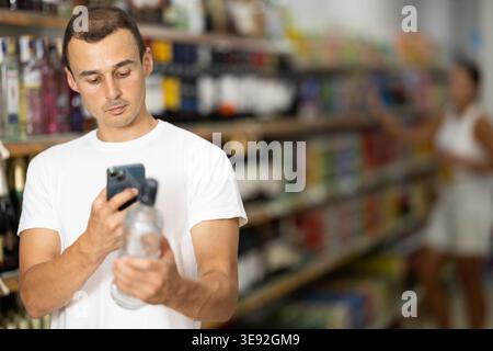 Man using smartphones to scan barcodes on bottles of alcoholic beverages Stock Photo