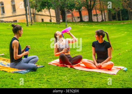 Women friends relaxing in park drinking water after yoga Stock Photo