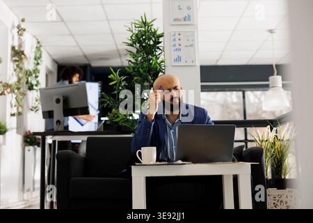Concentrated arab man thinking about project financial report while working on laptop in start up business office. Company employee rubbing head while solving marketing campaign problem Stock Photo