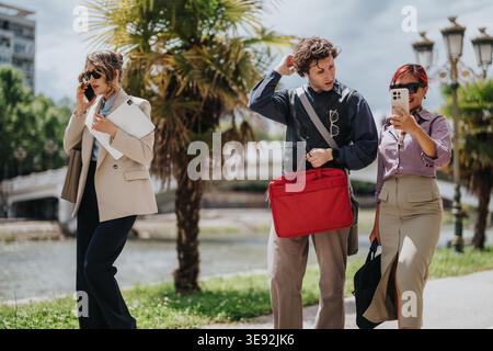 Business coworkers walking and talking outdoors by a riverside with laptops and briefcases Stock Photo