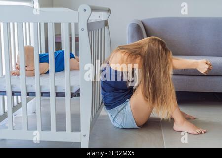 Very tired mother sitting by baby crib at home feeling exhausted. Sleep deprived mom caring for newborn at night. Parenting fatigue, motherhood stress Stock Photo