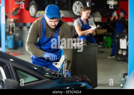 Professional mechanic man in uniform repairing car in auto repair garage Stock Photo
