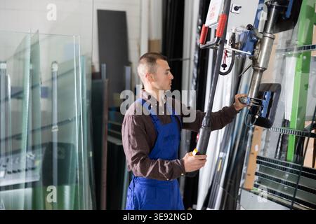 Male worker using control panel and lifting mechanism controls movement of window panes in an industrial workshop Stock Photo