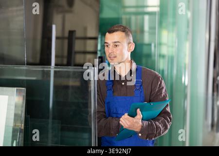 Worker inspecting glass panels and recording check results Stock Photo